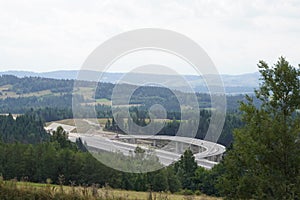 Construction of a modern overpass in mountains, high-speed concrete road in a mountainous area, a lot of tall trees on the slopes