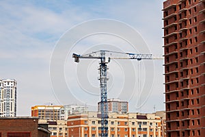 Construction of a multi-storey brick residential building of red color next to which stands a crane for lifting goods and