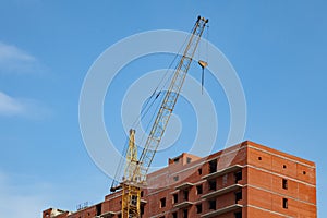 Construction of a multi-storey brick residential building of red color next to which stands a crane for lifting goods and