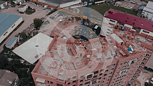 Construction of a multi-storey brick residential building of red color next to which stands a crane for lifting goods