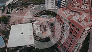 Construction of a multi-storey brick residential building of red color next to which stands a crane for lifting goods