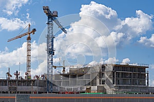 Construction of multi-storey building. High altitude cranes. Background - blue sky with clouds