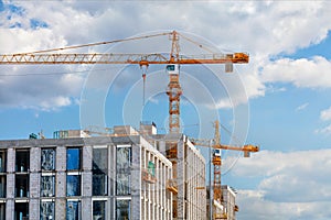 Construction of a multi-storey high-rise residential building using tower cranes against a blue slightly cloudy sky