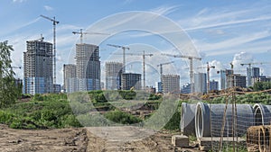 Construction of a multi-story residential buildings. Defocused foreground with young tree. Cranes work. Construction site