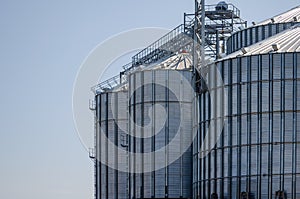 Construction of new cylindrical silos for grain storage. Metal silos are made of corrugated metal. A row of hand winches lifts the