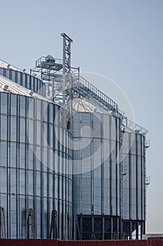 Construction of new cylindrical silos for grain storage. Metal silos are made of corrugated metal. A row of hand winches lifts the