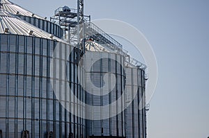 Construction of new cylindrical silos for grain storage. Metal silos are made of corrugated metal. A row of hand winches lifts the