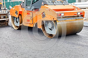 Construction of a new road. A large vibratory road roller paired with an asphalt paver paving and compacting the hot asphalt on