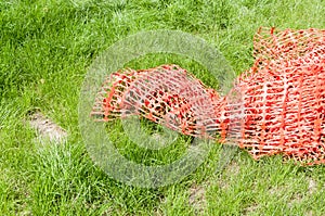 Construction orange safety net or fence, used as caution protective barrier, on the green grass