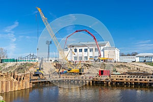 Construction of pedestrian bridge over river with special heavy machinery and equipment on sunny day. Working process of building