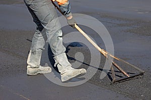 Construction road worker levelling fresh asphalt concrete