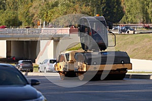 A construction roller rolls asphalt on a city highway. Special equipment is bypassed by cars. photo
