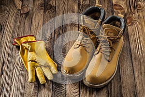 Construction safety tools yellow working gloves and leather working boots on vintage wooden background