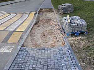 Construction of a sidewalk walkway from concrete paving slabs next to a pedestrian crossing and a speed bump