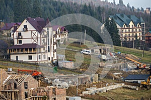 Construction site with building crane and new modern comfortable hotel house with shingled roof in ecological rural area on spruce photo