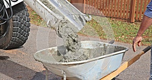 In a construction site, a concrete mixer truck is pouring wet cement into a wheelbarrow