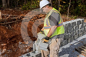 On the construction site, a contractor works on establishing a large block retaining wall that has just been constructed