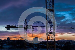 Construction site cranes against a fading sunset