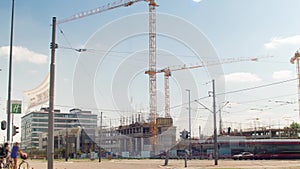 Construction site. Cranes moving, pedestrians crossing the road.