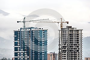 Construction site, cranes and multi-storey unfinished buildings over mist mountain background. Development building construction