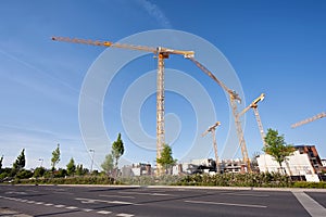 Construction site with cranes, next to a main street, on a blue, sunny day