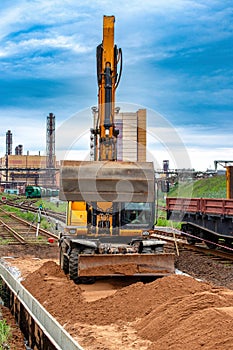 A construction site with a excavator lifting materials, surrounded by train tracks. Machinery and workers are visible on site