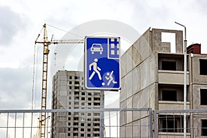 Construction site with high crane, gray block building house and blue and white living sector road sign.