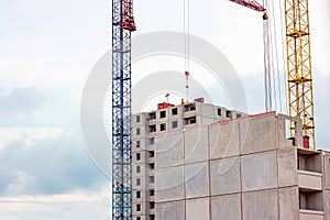 Construction site with the high cranes building a grey block house in the city.