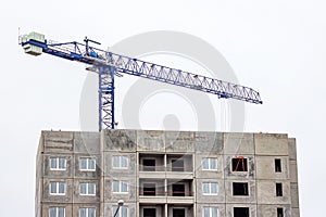 Construction site with the high cranes building a grey block house in the city.