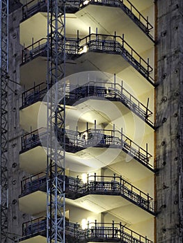 Construction site of a large high rise building at night with illuminated exposed stairs and floors with scaffolding and indus