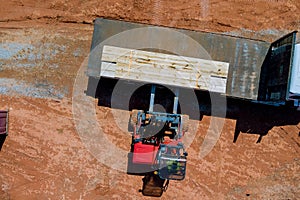 In a construction site, a lift manipulator unloads wooden building materials that have been delivered