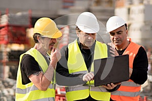 Construction site manager and two workers using pc laptop