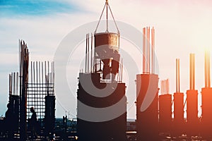 Construction site of modern building with silhouettes of workers busy pouring concrete in sunset light. Industrial