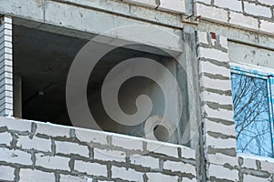 The construction site of a multi-storey residential building made of white brick against a blue sky background. View of the new