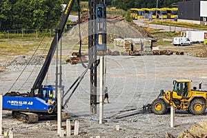 Construction site with pile driver and excavator at foundation work.