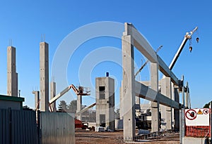 Construction site with pillars and the concrete block structure. Cherry pickers, telescopic crane and building equipment among