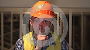 On a construction site, a worker or engineer or architect is making silence gesture