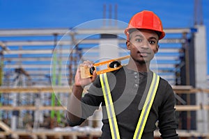 Construction site worker holding level tool and wearing red security hat helmet safety equipment