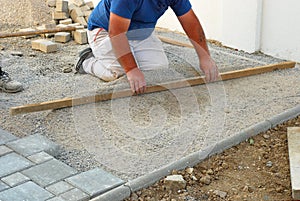 Construction site worker leveling the sand during installing concrete brick pavement