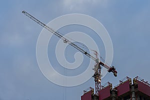 Construction tower crane next to a building under construction against the background of the blue sky with clouds. With