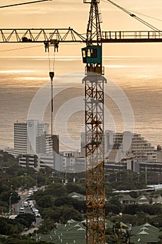 Construction tower crane over coastal town at sunrise