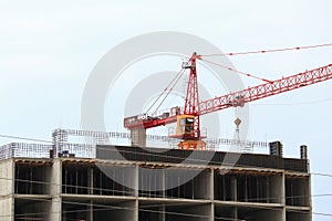 Construction tower crane over a multi-story apartment building under construction. Housing market, real estate, crisis