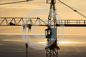 Construction tower crane overlooking dramatic ocean and sky at sunrise