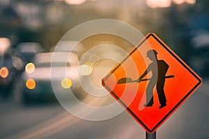 Construction warning sign on blur traffic road with colorful bokeh light abstract background