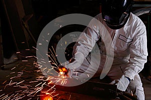 Construction welder in white uniform with protective helmet welding steel with spark in workshop. Industrial worker concept.