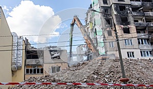 Construction work on the demolition of multi-storey apartments. Fence made of red and white warning tape. Excavator with hydraulic