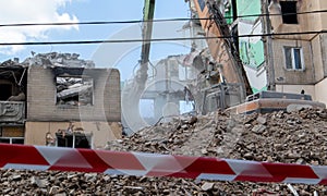 Construction work on the demolition of multi-storey apartments. Fence made of red and white warning tape. Excavator with hydraulic