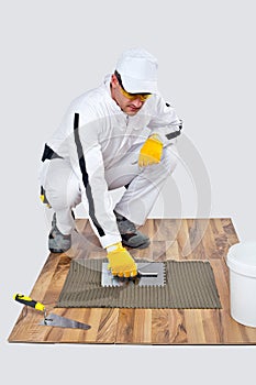 Construction worker applyes tile adhesive on wooden floor