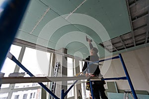 Construction worker assemble a suspended ceiling with drywall and fixing the drywall to the ceiling metal frame with