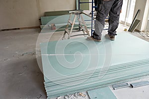 Construction worker assemble a suspended ceiling with drywall and fixing the drywall to the ceiling metal frame with